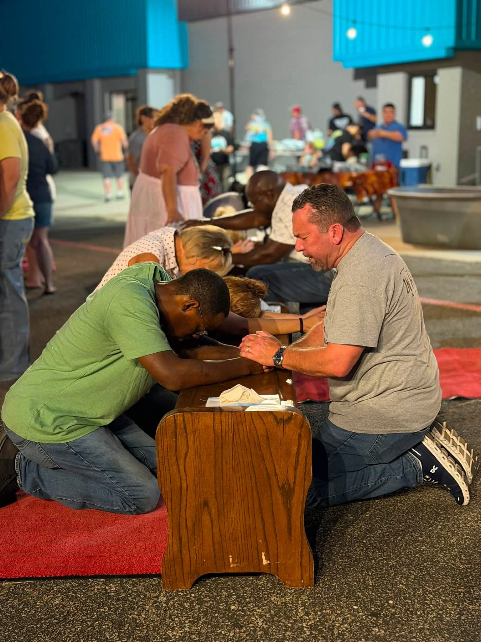Members of the community praying together at a wooden prayer bench.